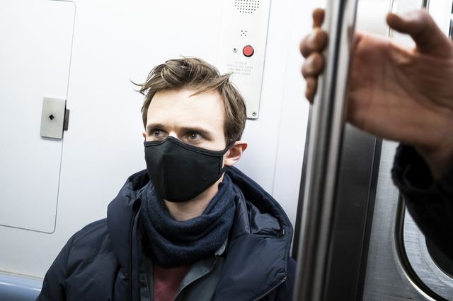 A man wears a mask to cover his face while riding the subway.